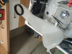 Biały plastikowy element pralki na tle narzędzi.
