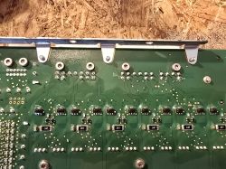 Fragment zielonej płytki PCB z widocznymi elementami elektronicznymi i śrubami mocującymi.