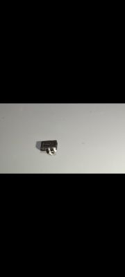Mały, czarny komponent elektroniczny z trzema metalowymi wyprowadzeniami leży na jasnej powierzchni.
