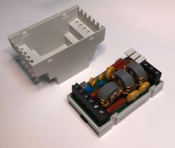 The image shows an opened plastic enclosure with an electronic circuit board featuring coils and capacitors.