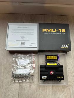 ECU Master PMU-16 kit: boxes, module in a plastic tray, and a bag of metal connectors on a wooden floor