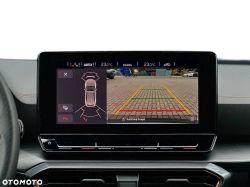 Car infotainment screen showing rear-view camera with parking guide lines on a paved lot