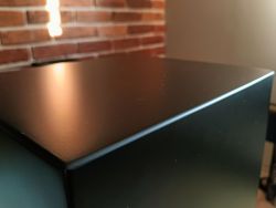 Zbliżenie na czarną półmatową obudowę kolumny głośnikowej z subtelnymi załamaniami światła na powierzchni.
