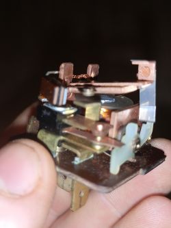 Zbliżenie na elektromechaniczny przekaźnik trzymany w palcach.