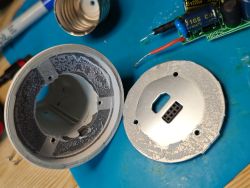 Rozebrana żarówka z gwintem E27, metalowa płytka z gniazdem i fragment płytki PCB na niebieskiej macie