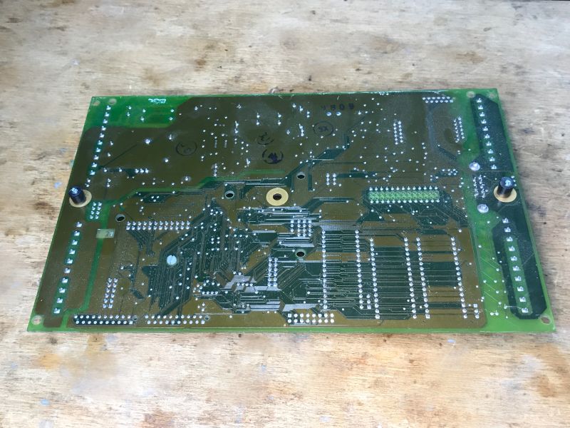 Underside of a green PCB with many traces and solder points on a wooden workbench