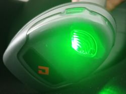 Zbliżenie na czytnik kodów kreskowych z migającą zieloną diodą.