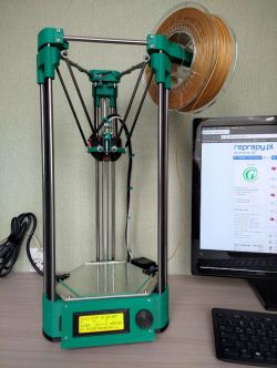 Delta 3D Printer on a Desk Delta 3D printer with green parts on a desk next to a monitor.
