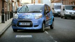 Niebieski samochód elektryczny, wynalazek Qualcomm, zaparkowany nad bezprzewodową ładowarką na ulicy.