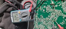 Multimetr cyfrowy mierzący napięcie na płytce drukowanej z elementami elektronicznymi.