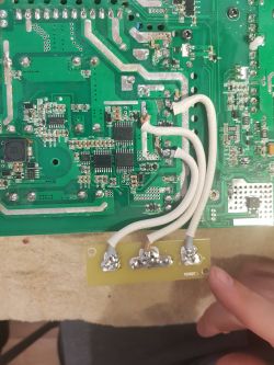 Close-up of a circuit board with white wires soldered onto it.