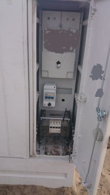 Otwarta szafka elektryczna z licznikiem oraz wyłącznikami i rozłącznikiem pod przezroczystą osłoną