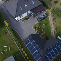 Zdjęcie z lotu ptaka pokazujące dom z panelami fotowoltaicznymi i miejscem zaznaczonym na czerwono.