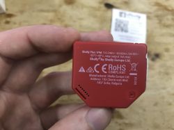 Red Shelly Plus 1PM module held in a hand, showing technical info on back