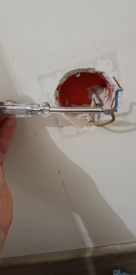 Widok wnętrza puszki elektrycznej z trzema przewodami: brązowym, niebieskim i żółto-zielonym. Obok śrubokręt z probówką.