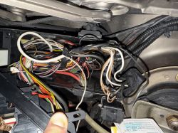 Zbliżenie na skrzynkę bezpieczników w komorze silnika samochodu z widocznymi kablami i przekaźnikami.