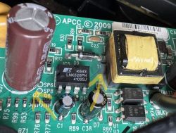 Zbliżenie na płytkę drukowaną UPS APC z widocznym układem LNK520PN, kondensatorem elektrolitycznym i transformatorem.