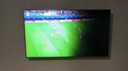 Telewizor na ścianie wyświetlający mecz piłki nożnej z problemem podświetlenia.