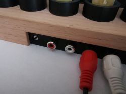 Close-up of RCA jacks mounted on a wooden enclosure with connected cables.