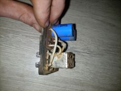 Ręka trzymająca rosyjski 4-pinowy przerywacz kierunkowskazów z widocznymi przewodami i niebieskim kondensatorem.