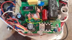 Close-up of PCB with damaged via under resistors near the triac, highlighted in yellow