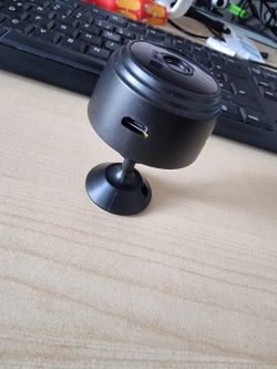 Black, small Wi-Fi 1080p camera on a desk with a keyboard in the background.