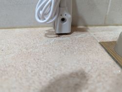 Close-up of a sensor mounted by the wall with an attached cable and a visible opening for the LED.