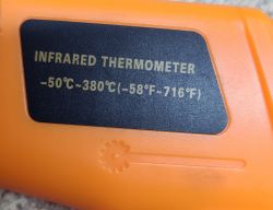 Zbliżenie na termometr bezdotykowy z celownikiem laserowym, na którym widać zakres temperatur: -50°C do 380°C.
