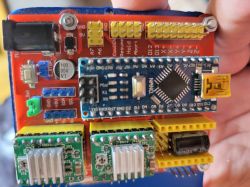 Zbliżenie na płytkę Arduino Nano zamontowaną na shieldzie CNC z widocznymi złączami, pinami i sterownikami silników krokowych.