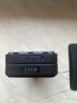 Małe czarne urządzenie z portem USB oraz złączem do ładowania, widok z bliska.