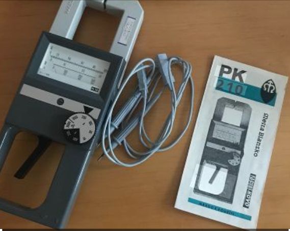 Miernik cęgowy PK 210 z przewodami pomiarowymi i instrukcją na drewnianym blacie