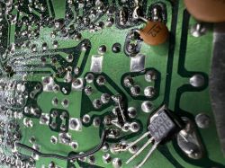 Spód zielonej płytki PCB z licznymi lutami, przewodem i elementami: kondensator oraz dioda z oznaczeniem 1N4004