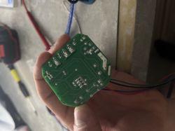 A person holds a green printed circuit board with visible tracks and a few electronic components.