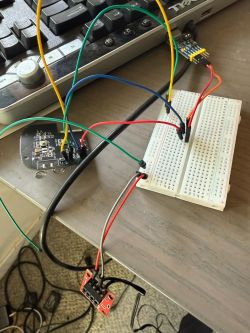 A breadboard with connected jumper wires, a UART module, and a push button, all set on a desk next to a keyboard.