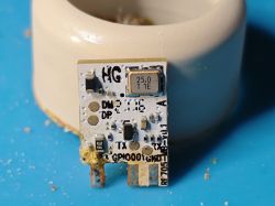 Close-up of an electronic module with a 25.0 MHz crystal oscillator, mounted vertically in front of a ceramic base.