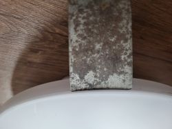 Rusty knife blade leaning against a white plate on a wooden surface