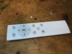 White remote control with several buttons lying on a wooden table.