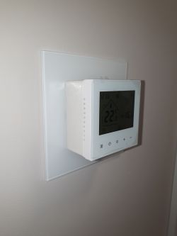 White Wi-Fi thermostat on wall, mounted on a transparent glass wall plate