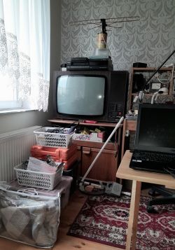 Stary telewizor CRT Helios Monitor TC706A z anteną na górze, obok koszyki i sprzęt elektroniczny w pokoju.