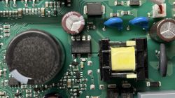 Zbliżenie na płytkę drukowaną z komponentami elektronicznymi, w tym kondensatorami, rezystorami i transformatorem impulsowym.