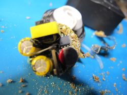 Close-up of a damaged and partially disassembled electronic power supply with visible components and burn residues.