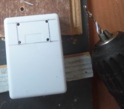 White plastic casing marked for drilling with holes and electric drill nearby