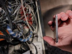 Osoba trzymająca kartę PCMCIA PC Card 16 w pobliżu plątaniny kabli.