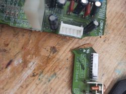 Two broken pieces of green printed circuit board (PCB) with connectors and electronic components on a wooden surface.