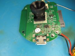 Circuit board with camera lens and micro USB port Printed circuit board with electronic components, a micro USB port, and a camera lens on a blue surface.