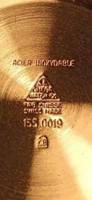 Zbliżenie na wnętrze koperty zegarka Omega z widocznym napisem „ACIER INOXYDABLE” i numerem referencyjnym 155.0019.