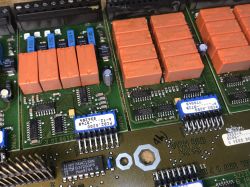 Close-up of PCB modules with orange relays, integrated circuits, and blue DIP switches