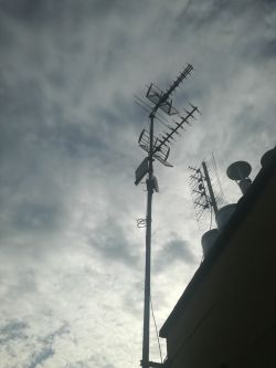 Antena siatkowa zamontowana na wysokim maszcie w tle z chmurami.