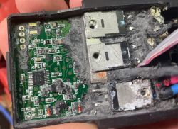 Zbliżenie na płytkę PCB w czarnej obudowie, częściowo zalaną czarną masą, z metalowymi elementami mocy