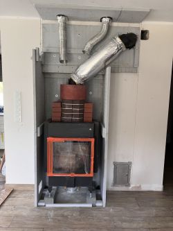 Kominek z widoczną rurą kominową pokrytą materiałem izolacyjnym, z zabudową z płyt Skamol.